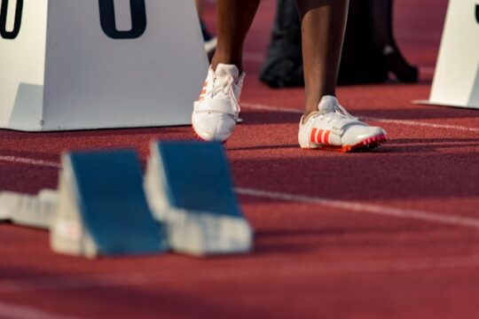 Person at the start of a 100m race, showing their feet and the race blocks